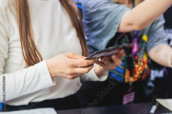 Fototapeta Process of checking in on a conference congress forum event, registration desk table, visitors and attendees receiving a name badge and entrance wristband bracelet and register electronic ticket