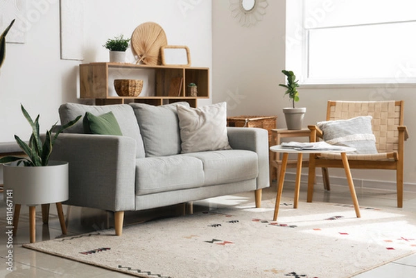 Fototapeta Interior of cozy living room with sofa, shelving unit and houseplants near white wall