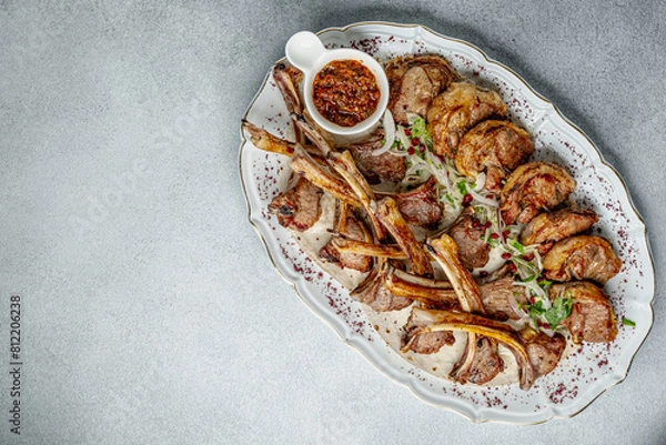 Fototapeta The photo shows roasted ribs neatly laid out on a white platter with ornaments. The ribs are well fried and garnished with herbs. The background of the image is a textured gray table, which contrasts 