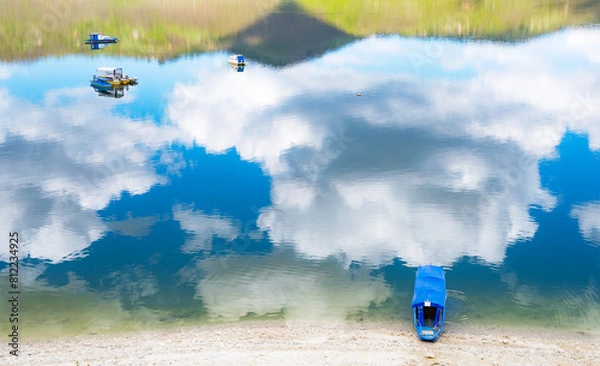 Obraz Lanscape image of boat floating on crisp mountaing lake water covered by cloud reflexions.