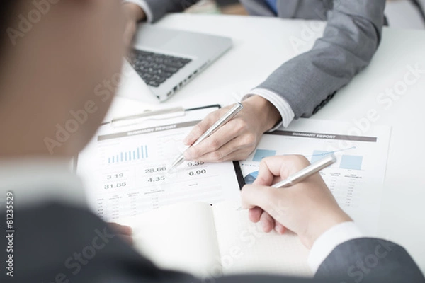 Fototapeta Two businessmen looking at report and having a discussion in off