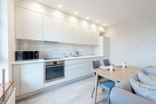 Fototapeta Classic White Kitchen Interior and Dinning Table. Oven, Kettle, Microwave and Glass. Plates on the Table. Minimalistic Interior Design