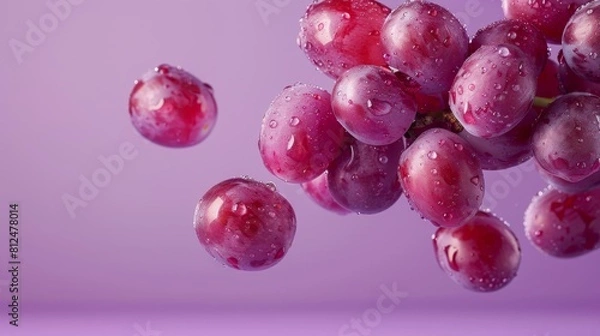 Fototapeta A cluster of grapes with refreshing water droplets floating against a soft purple background, highlighting their vibrant color.