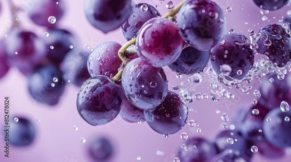 Fototapeta Lush purple grapes captured with sparkling water droplets against a soft pink background, emphasizing freshness and vitality.