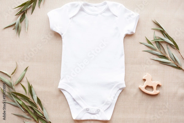 Fototapeta Mockup of white baby bodysuit on linen with greenery and toy. Blank baby clothes template in farmhouse style, flat lay.