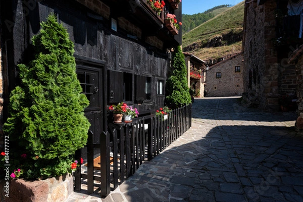 Obraz Small medieval village with cobblestone streets and a stone building with a black fence with potted colorful flowers, Barcena Mayor, Saja-Besaya Natural Park, Cantabria, Spain.