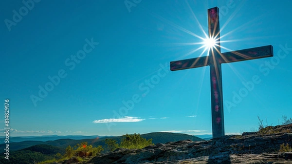 Fototapeta A Christian cross on a high plateau during a clear day, with the unobstructed sun illuminating the cross and the bright blue sky providing a vivid canvas behind it.