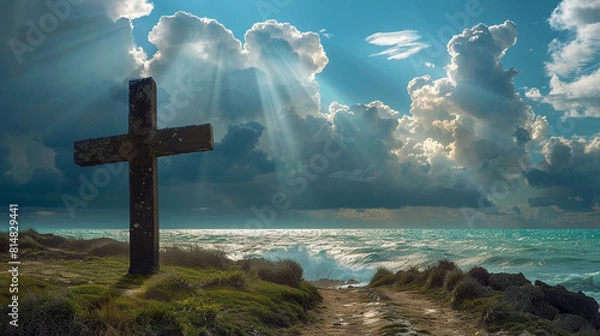 Obraz A Christian cross on a coastal path, with a stormy sea in the background and dramatic clouds parting just enough for beams of sunlight to highlight the cross.