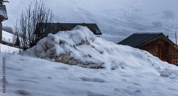 Fototapeta Tas de neige entassé devant des chalets en hiver dans les Alpes à la Toussuire par une journée avec du brouillard