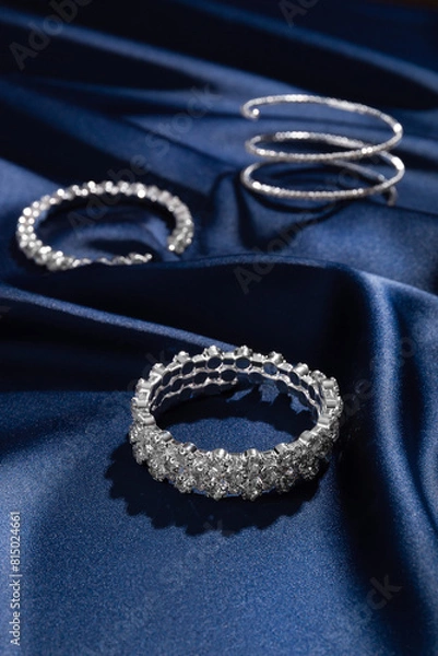 Fototapeta Bracelets with diamonds on a background of blue silk. Expensive jewelry. Natural gems. Top view. Space for text.
