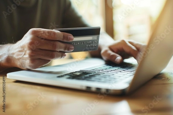 Fototapeta A person holding their credit card, about to make an online shopping order on the laptop computer in front of them.