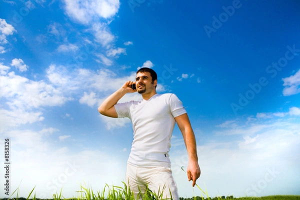 Fototapeta Man at the phone in the field under blue sky. In white dress