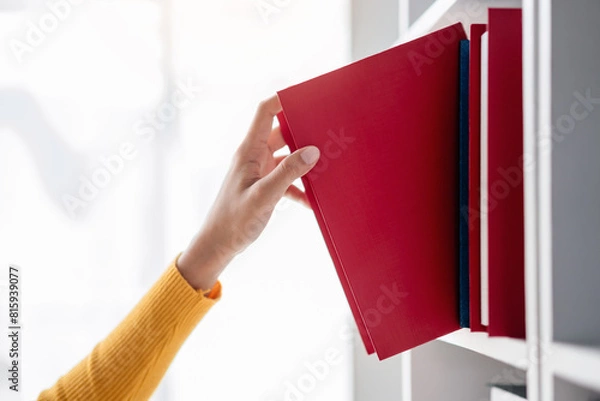 Obraz A person is reaching for a red book on a shelf