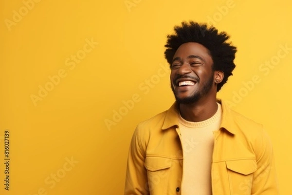 Fototapeta Portrait of a glad afro-american man in his 20s laughing isolated in soft yellow background