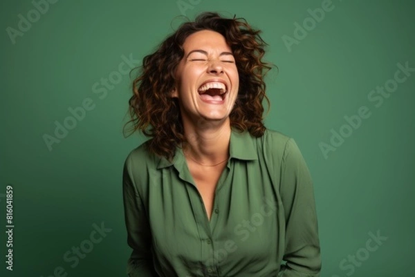 Fototapeta Portrait of a satisfied woman in her 30s laughing in front of soft green background