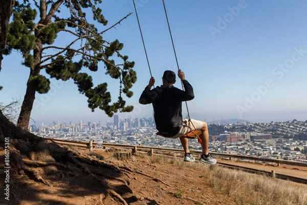 Fototapeta A man swings under a tree on the hill of Burnal Heights in San Francisco, California