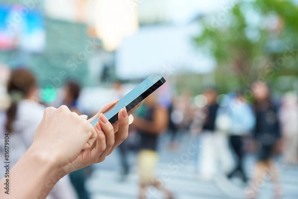 Fototapeta 繁華街でスマートフォンを操作する女性の手元