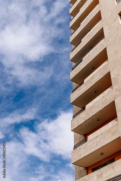 Fototapeta Vertical shot of modern building with balconies against a blue sky, showcasing urban architecture