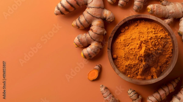 Fototapeta Top view of organic turmeric powder in a bowl with fresh turmeric roots scattered on a warm, earth-toned surface