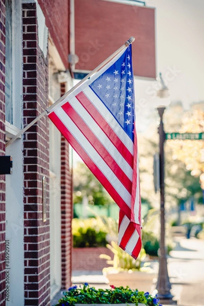 Obraz An American flag is hanging from a building on a traditional street in a small town.