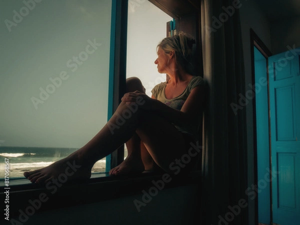 Fototapeta Woman sitting on a window looking at the sea
