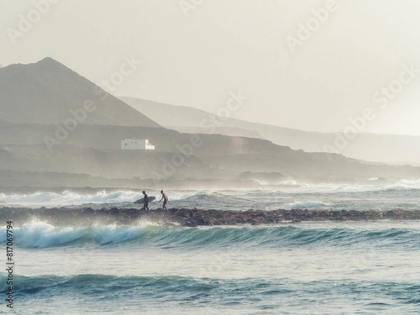 Fototapeta Surfers returning tired to the beach amidst the waves