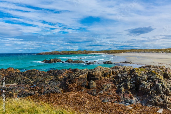 Fototapeta Balevullin Beach, Isle of Tiree, Scotland with rocks covered in dried seawee, marram grass, blue sky and beautiful beach.  Horizontal.  Space for copy