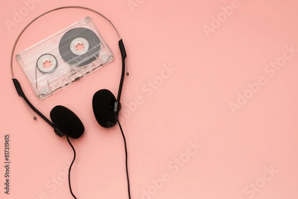 Fototapeta A pair of 1990's style headphones and and cassette tape on a pink background retro vintage music concept image