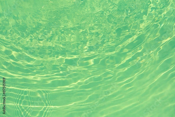 Fototapeta Green water with ripples on the surface. Defocus blurred transparent blue colored clear calm water surface texture with splashes and bubbles. Water waves with shining pattern texture background.
