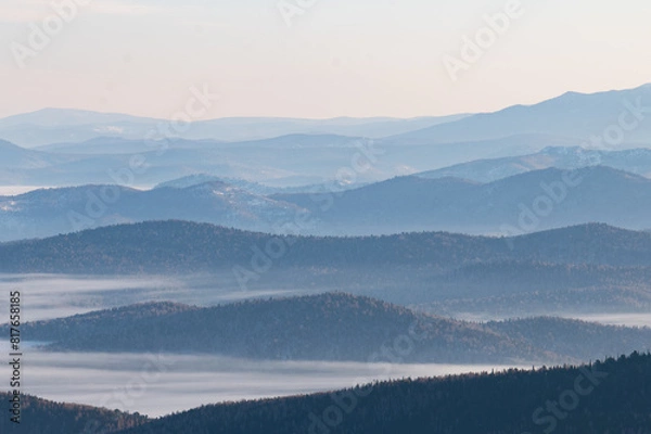 Fototapeta Aerial perspective in the mountains with peaks overgrown with forest and fog between them stretching into the distance to the horizon