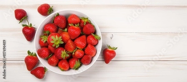 Fototapeta Top view copy space image of a white wooden background with a heap of fresh strawberries in a bowl