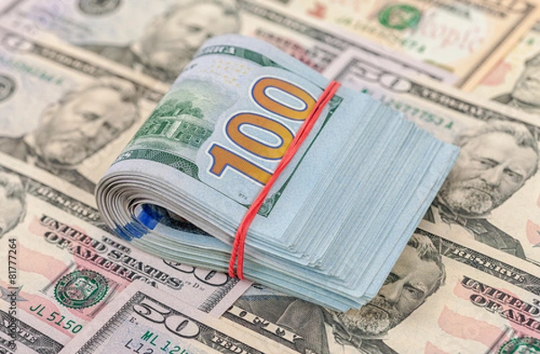 Obraz Folded dollar bills wrapped by rubber lying over  banknotes