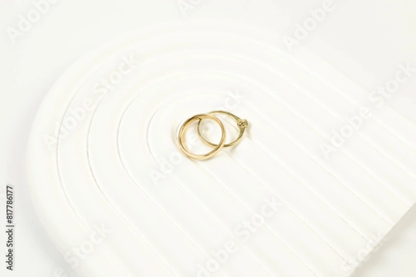 Fototapeta Top view of wedding gold rings on white background. Abstract wedding composition, white arch tray, podium. Copy space, flat lay.