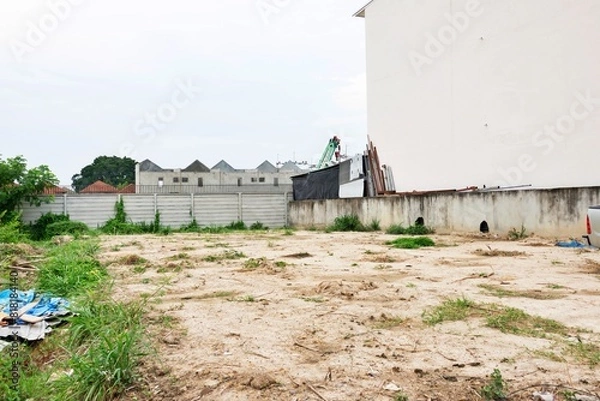 Obraz A vacant lot with a fence and a building in the background. The lot is empty and has no people or vehicles,land for sale