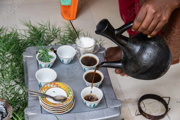 Fototapeta A jebena sits on a grass-covered table with small, handle-less cups arranged around it. Roasted coffee beans, a mortar and pestle, and incense smoke create a traditional Ethiopian coffee ceremony