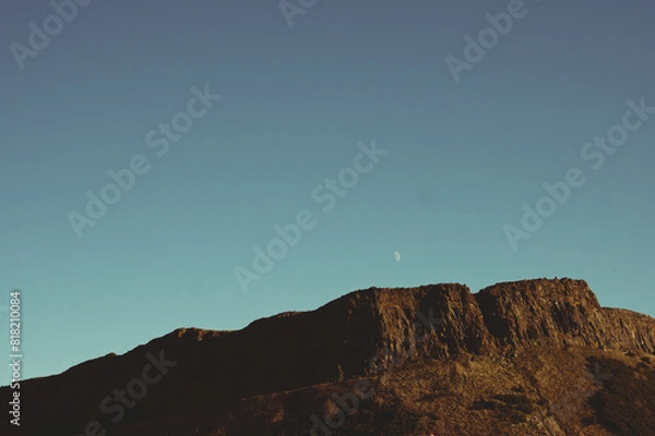 Fototapeta Moon rising over Salisbury Crags cliffs in Edinburgh, Scotland