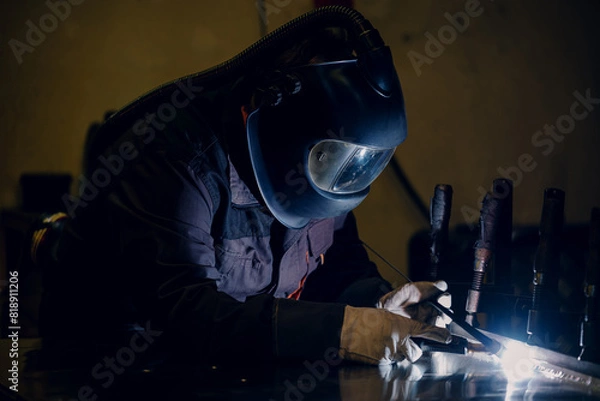 Fototapeta Man worker working with a metal product and welding it with a arc welding machine in a workshop. Industrial manufacturing. Welding metal part in a factory.