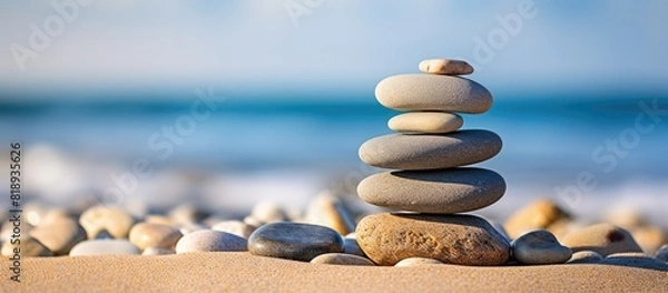 Fototapeta A zen symbol in the form of a pyramid of stones resting on sandy ground representing harmony and balance The image also includes the serene backdrop of the ocean with a closeup of a tower of sea pebb