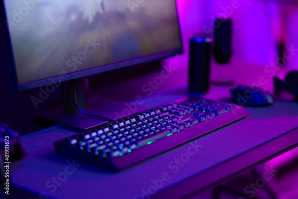 Fototapeta Modern gaming setup with keyboard, mouse, and monitor in a dimly-lit room with purple lighting