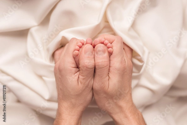 Obraz Baby feet of a newborn in dad's hands. On a white background.	