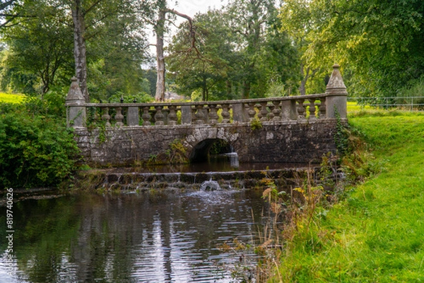 Obraz the stone bridge has two small fountains running under it and the grass is beside