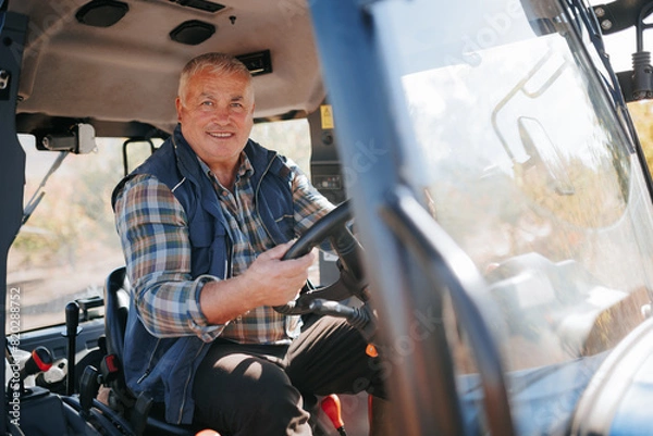 Fototapeta In Control Elderly Farmer Operating Tractor in Agricultural Setting