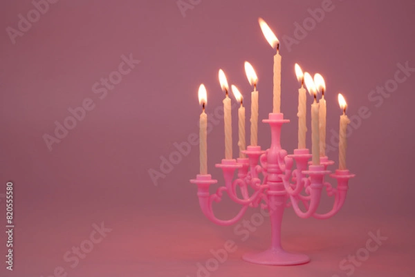 Fototapeta Pink candelabra with many white burning candles on pink background. Copy space for text.	