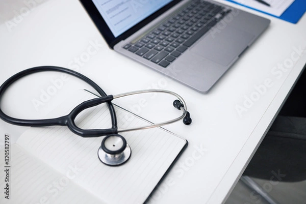 Fototapeta Stethoscope, laptop and desk for healthcare background, medical research and hospital services or planning. Computer, heart equipment and clinic information, cardiology or telehealth in empty office
