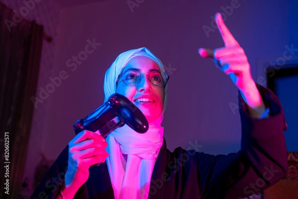 Fototapeta Gamer, headphones and portrait of woman in home at night in neon light for web esports. Gaming face, cyber technology and gen z female with controller playing online games and video game in house..