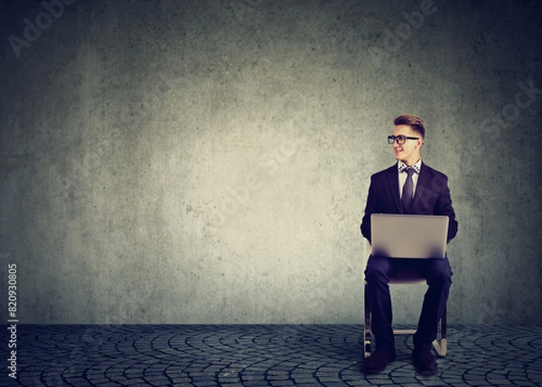 Fototapeta Happy businessman sitting on a chair with laptop computer looking to the side 