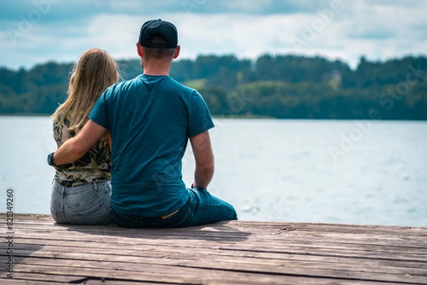 Fototapeta A couple sits on a wooden bridge by the lake in warm summer weather. Thinking one on one with nature.
