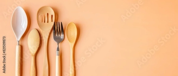 Fototapeta Set of wooden kitchen utensils on a peach background, ideal for culinary-themed design, restaurant decor, or food blogs.