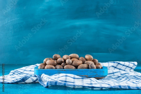 Fototapeta Pecan nuts in a wooden plate on a tea towel , on the blue background