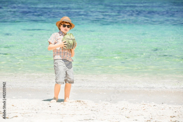 Fototapeta Happy young boy staying on beautiful ocean beach wearing hat and